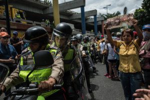 Manifestantes enarbolan pancartas de protesta contra la situación económica de Venezuela mientras los oficiales de policía se despliegan en las calles, en junio. Credit Meridith Kohut para The New York Times
